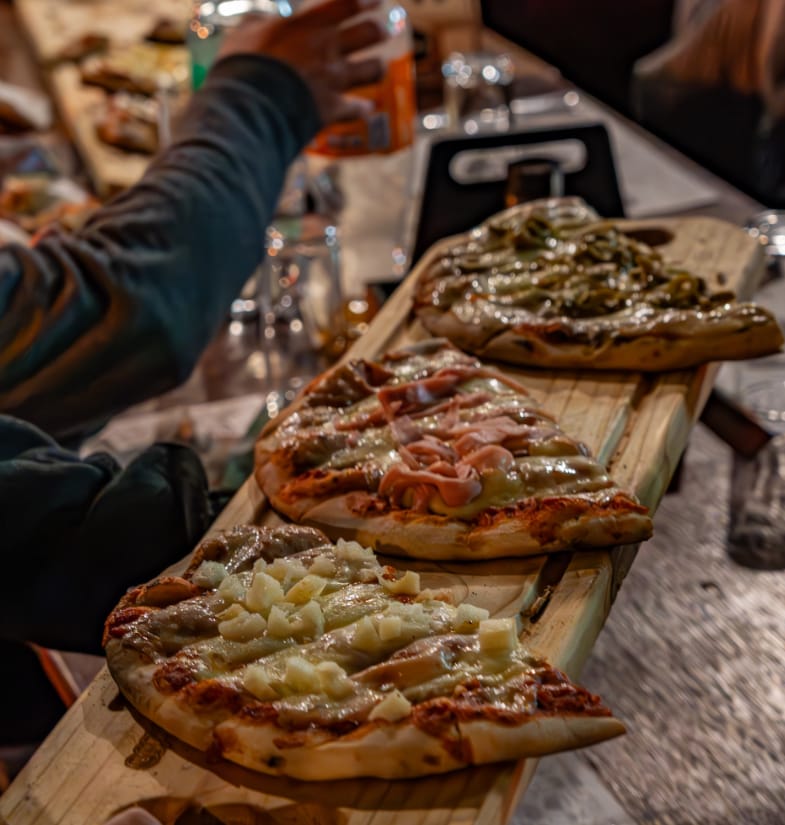 Tres pizzas recién salidas del horno servidas sobre una tabla larga de madera